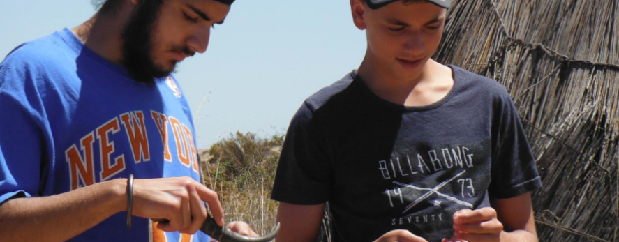 Two boys standing by a hut using a tool